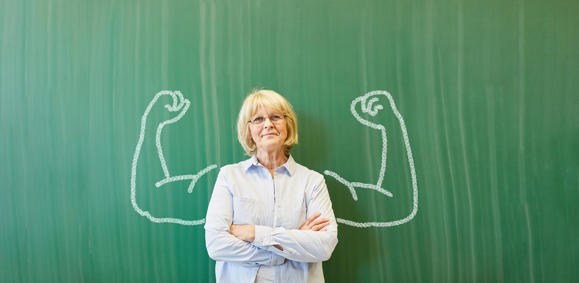 Strong,Senior,Teacher,With,Chalk,Muscles,In,Front,Of,Chalkboard