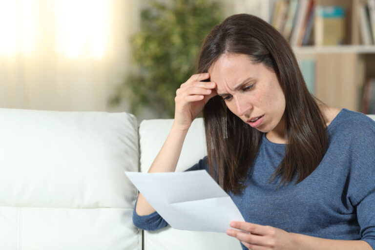 Worried,Woman,Reading,A,Letter,Sitting,On,A,Couch,In