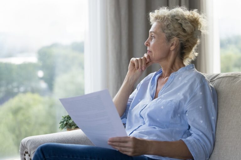 Thoughtful,Mature,Woman,Sitting,On,Sofa,At,Home,,Hold,Papers