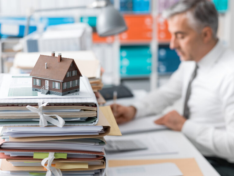 Real,Estate,Agent,Working,In,The,Office,And,Piles,Of