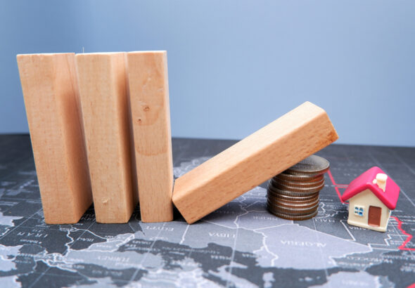 Wooden,Dominoes,Fall,On,A,Pile,Of,Coins,With,House