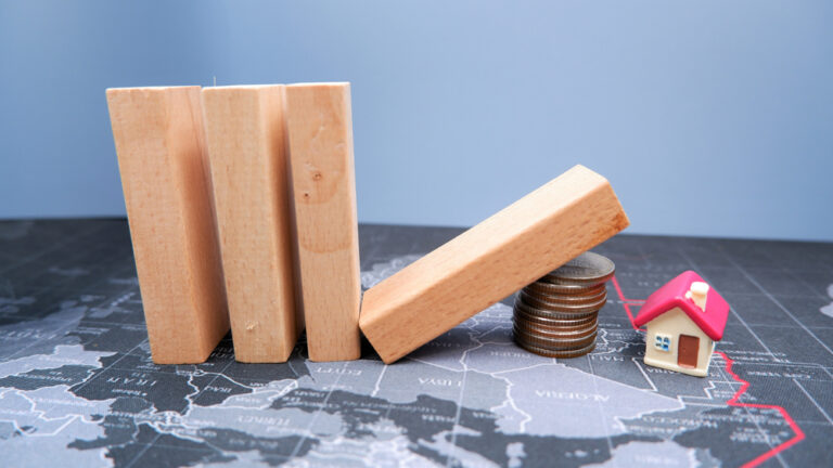 Wooden,Dominoes,Fall,On,A,Pile,Of,Coins,With,House