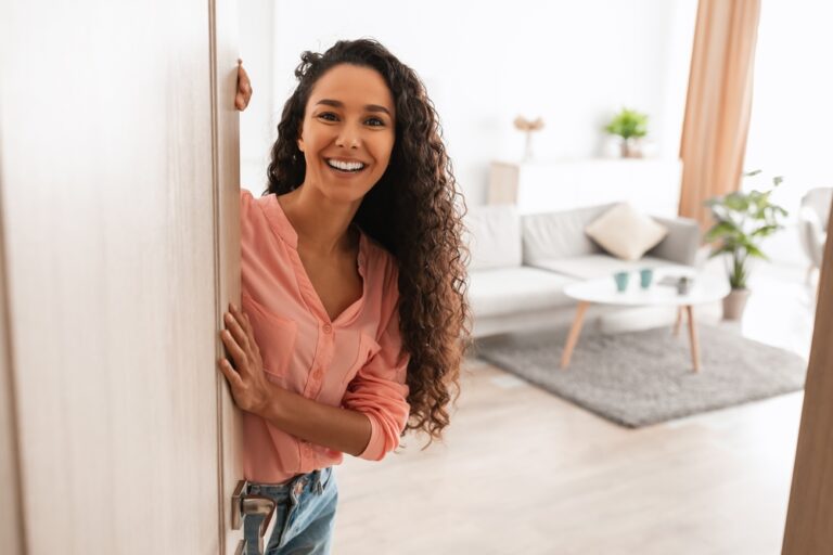 Welcome.,Portrait,Of,Cheerful,Woman,Standing,In,Doorway,Of,Modern