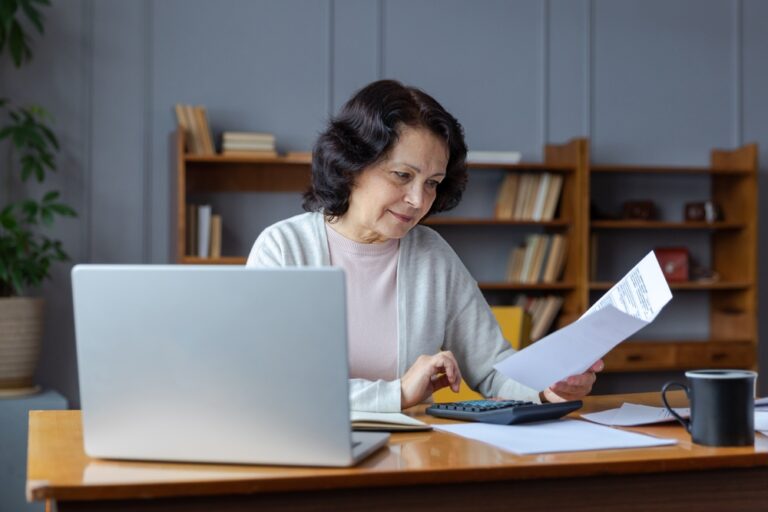 Middle,Aged,Senior,Woman,Sit,With,Laptop,And,Paper,Document.