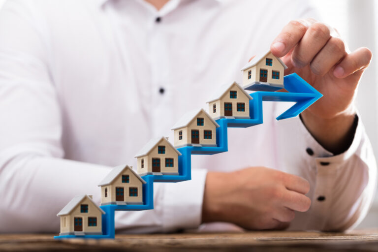 Close-up,Of,A,Businessman's,Hand,Placing,House,Models,On,Increasing