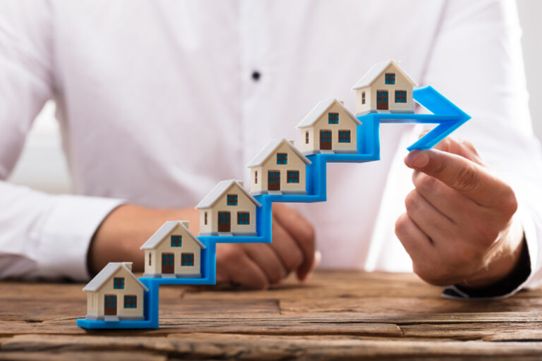 Close-up,Of,A,Businessman's,Hand,Placing,House,Models,On,Increasing