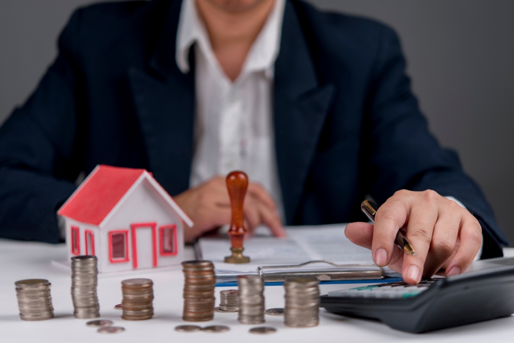 Businessman,Calculating,Real,Estate,Investment,,With,House,Model,,Coins,,And