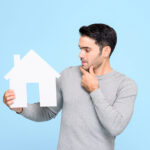 Young,Man,Looking,At,House,Model,And,Thinking,Isolated,On
