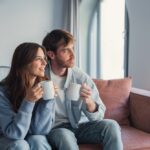 A,Loving,Couple,Relaxes,On,The,Couch,With,Hot,Drinks