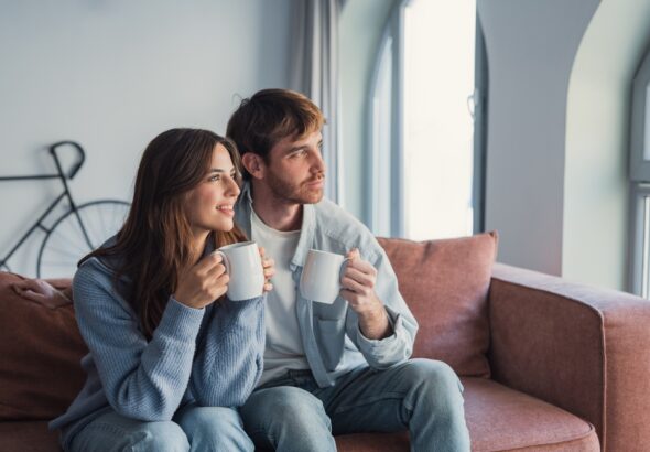 A,Loving,Couple,Relaxes,On,The,Couch,With,Hot,Drinks