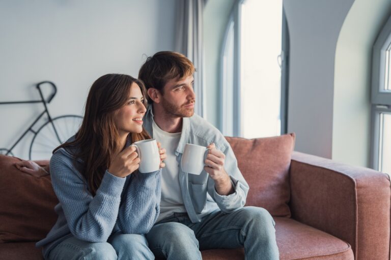A,Loving,Couple,Relaxes,On,The,Couch,With,Hot,Drinks