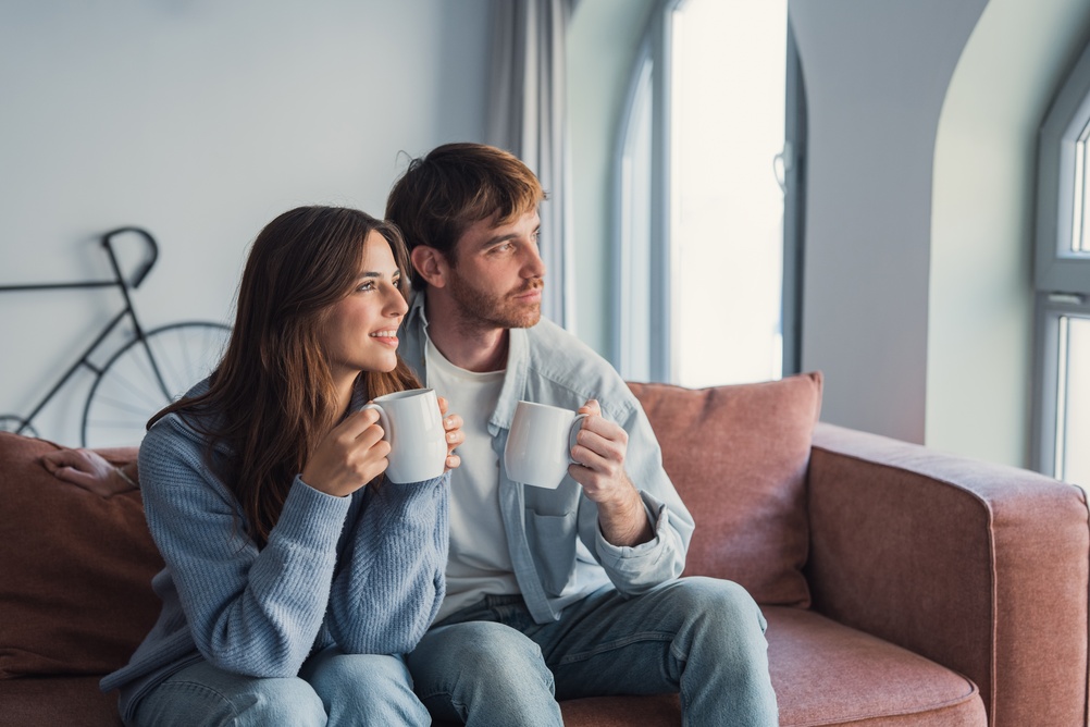 A,Loving,Couple,Relaxes,On,The,Couch,With,Hot,Drinks