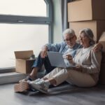 Elderly,Couple,Sits,On,The,Floor,Surrounded,By,Cardboard,Boxes,