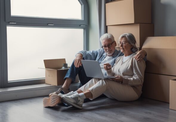 Elderly,Couple,Sits,On,The,Floor,Surrounded,By,Cardboard,Boxes,