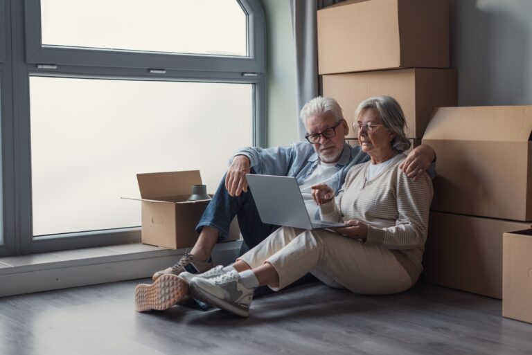 Elderly,Couple,Sits,On,The,Floor,Surrounded,By,Cardboard,Boxes,