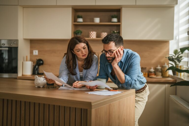 Young,Couple,In,Their,Kitchen,Reviewing,Important,Bills,And,Documents,