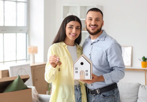 Happy,Young,Couple,With,House,Figure,And,Key,To,Rented