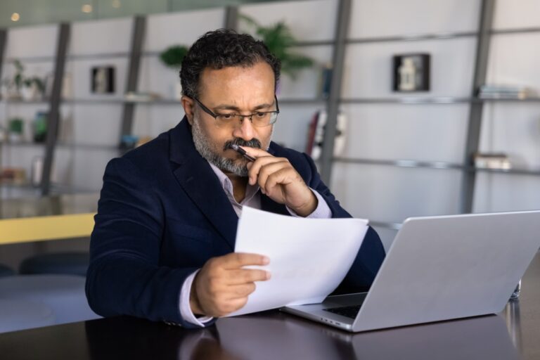 Thoughtful,Frowning,Senior,Indian,Businessman,Reading,Paper,Document,At,Laptop,