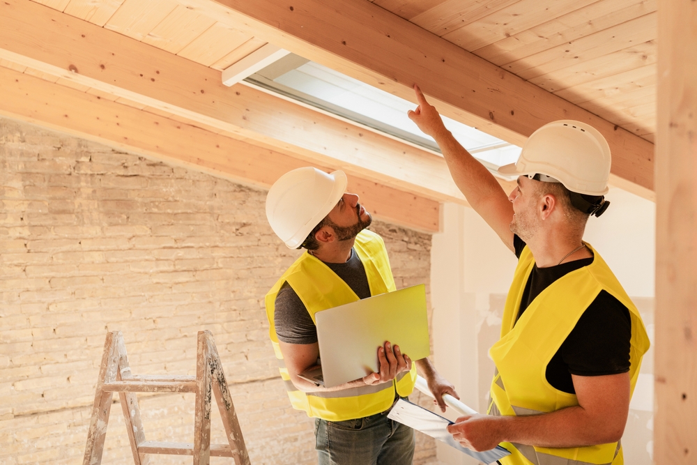 Two,Male,Construction,Workers,Using,Laptop,Inspecting,Wooden,Beams,In