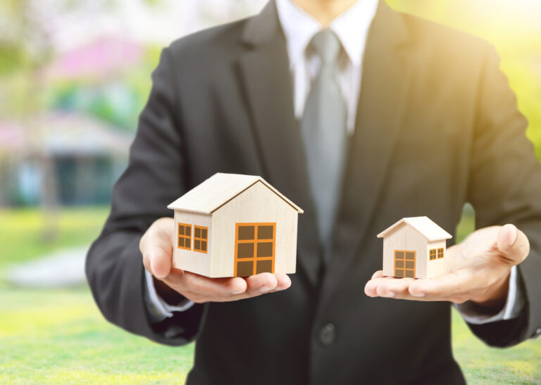 Businessman,Hold,Big,And,Small,Houses,On,Hand
