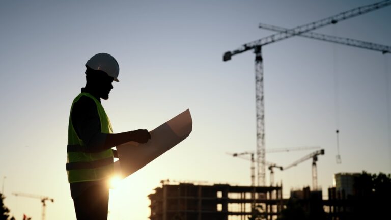 Builder,,Engineer,Or,Architect,In,Helmet,Checking,Drawings,At,Construction