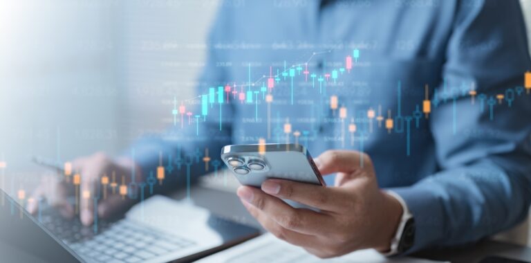 A,Person,Analyzing,Investment,Data,On,A,Smartphone,And,Laptop