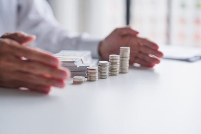 Asian,Businessman,Protecting,Growing,Pile,Of,Coins,With,Both,Hands,